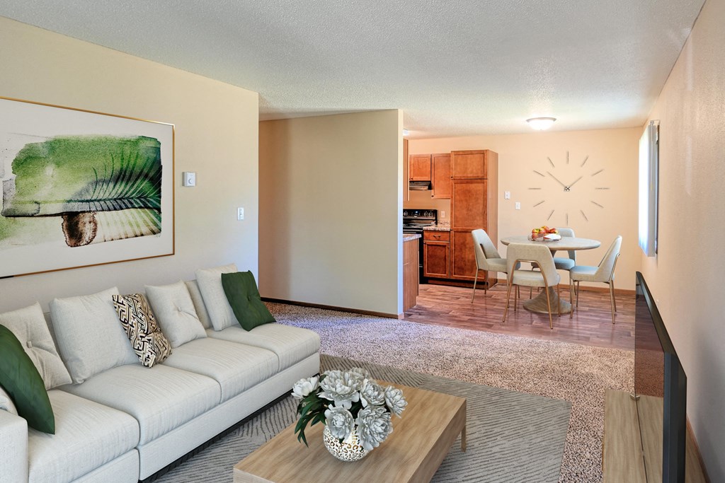 a living room with a couch and a coffee table in front of a dining room. Grand Forks, ND Madison Apartments