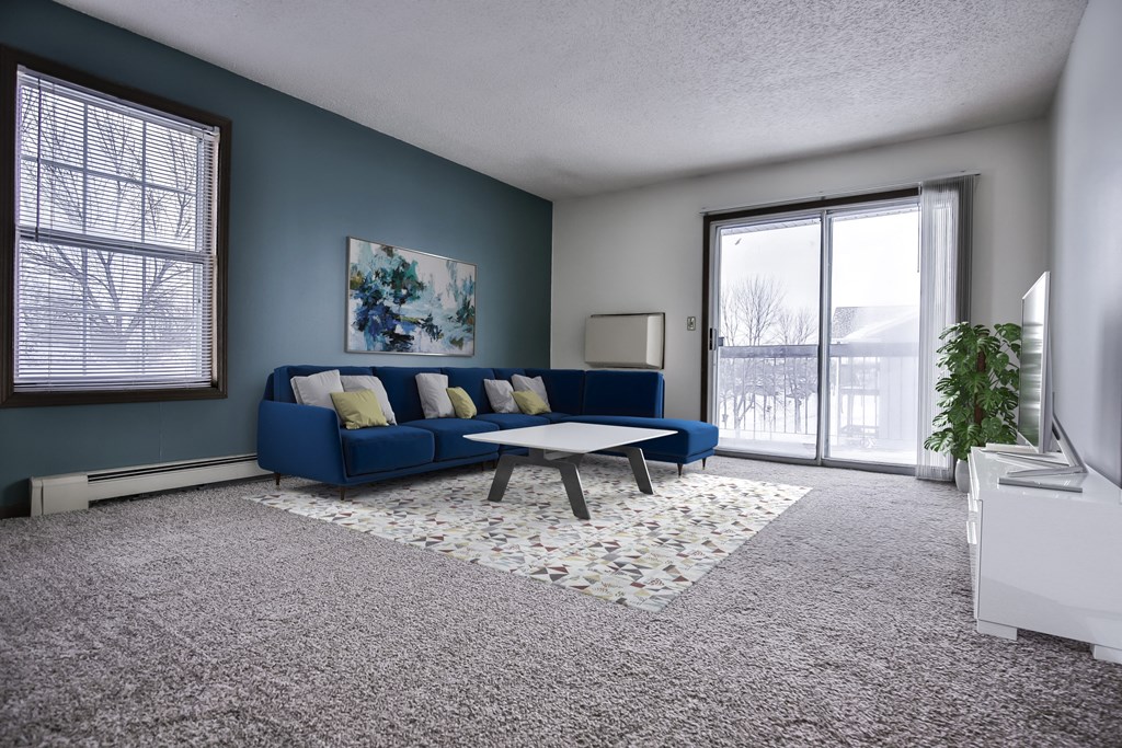 Grand Forks Kremer Apartments. A living room with a blue couch and coffee table in front of a sliding glass door