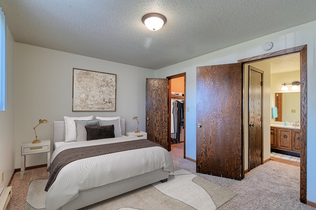 Grand Forks, ND Roughrider Apartments. a bedroom with a large bed and a bathroom in the background