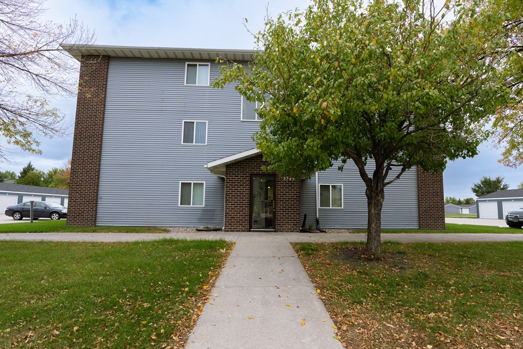Grand Forks, ND Southview III Apartments. The front of a blue building with a sidewalk and a tree
