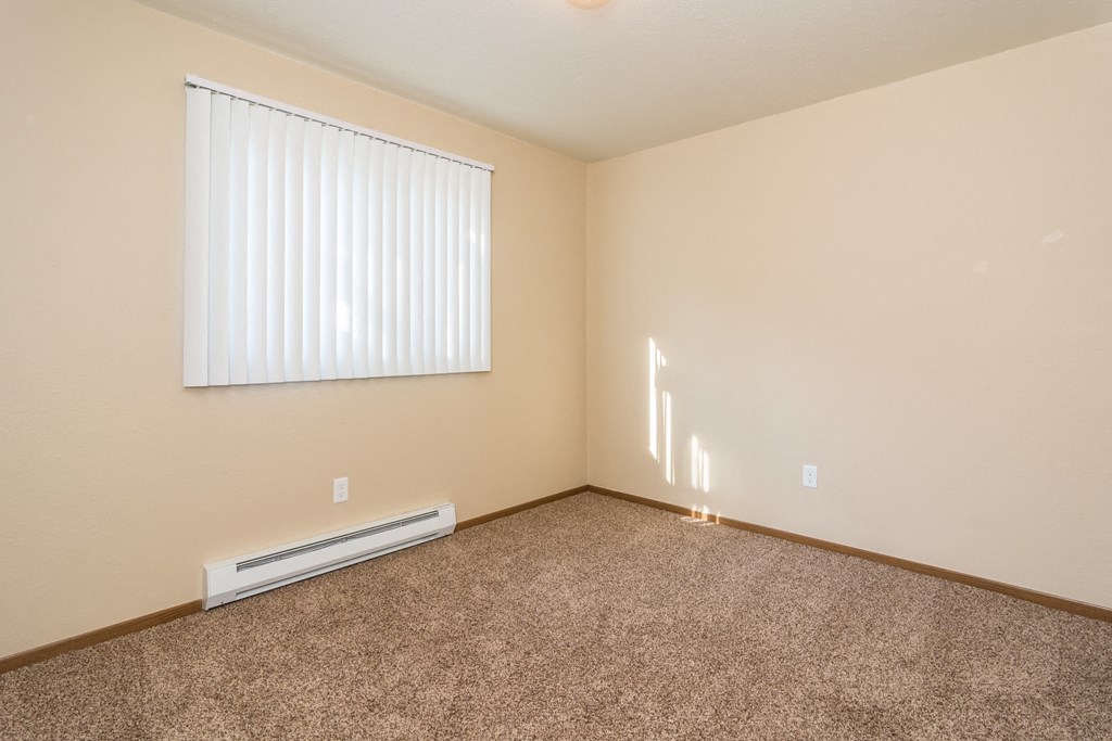 Grand Forks, ND Stanford Court Apartments. A kitchen with black appliances and a living room in the background a bedroom with a large window and a carpeted floor