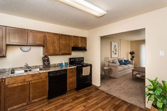 Grand Forks, ND Stanford Court Apartments. A kitchen with black appliances and a living room in the background - Photo Gallery 3