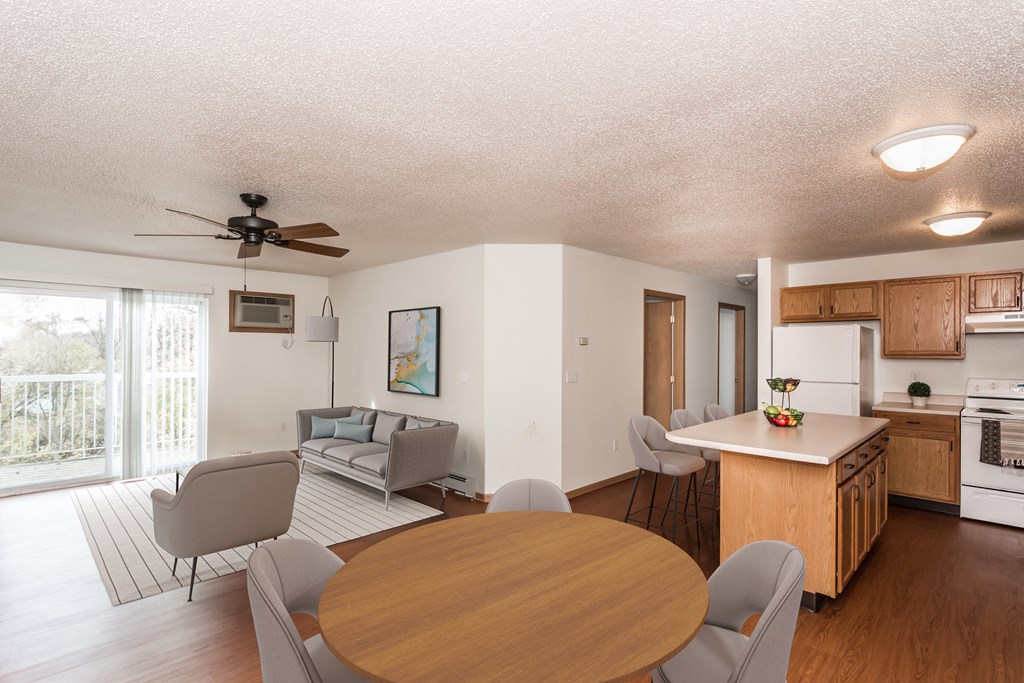 Grand Forks, ND Vista Apartments. A living room and dining room with a couch, chair, and table with the kitchen in the background.