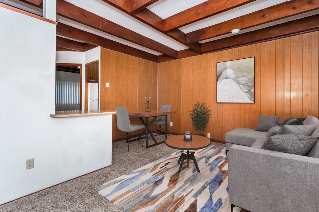 Grand Forks, ND Washington Apartments. A living room with wood paneling and a beamed ceiling with a couch and dining area in the background