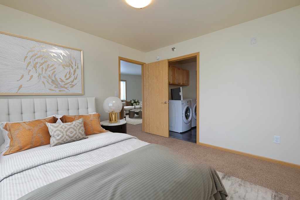 a bedroom with a bed and a washer and dryer in a room. Moorhead, MN Sandy Creek Apartments
