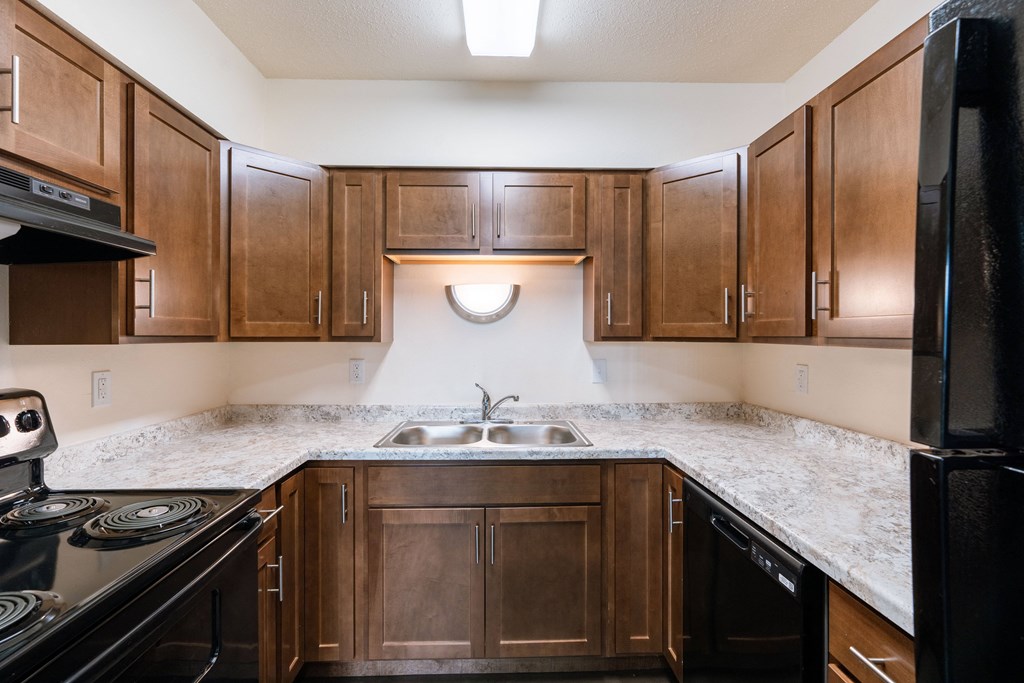 an empty kitchen with wooden cabinets and granite counter tops. Moorhead, MN South Park Apartments