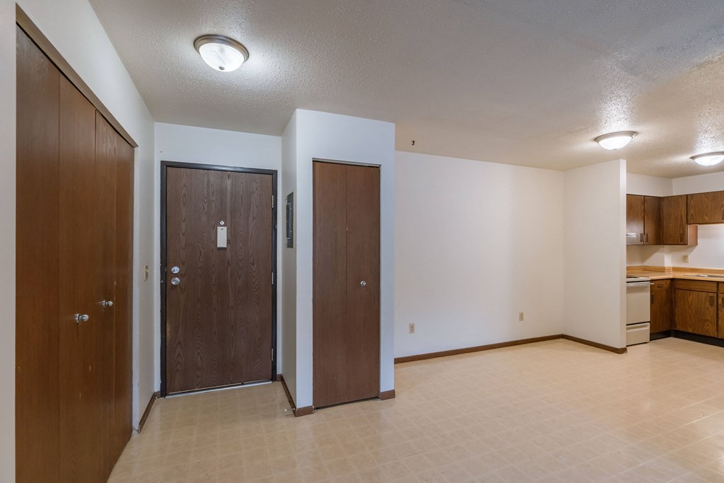 an entry door with a couple closets and a dining room and kitchen in the background. Moorhead, MN South Park Apartment
