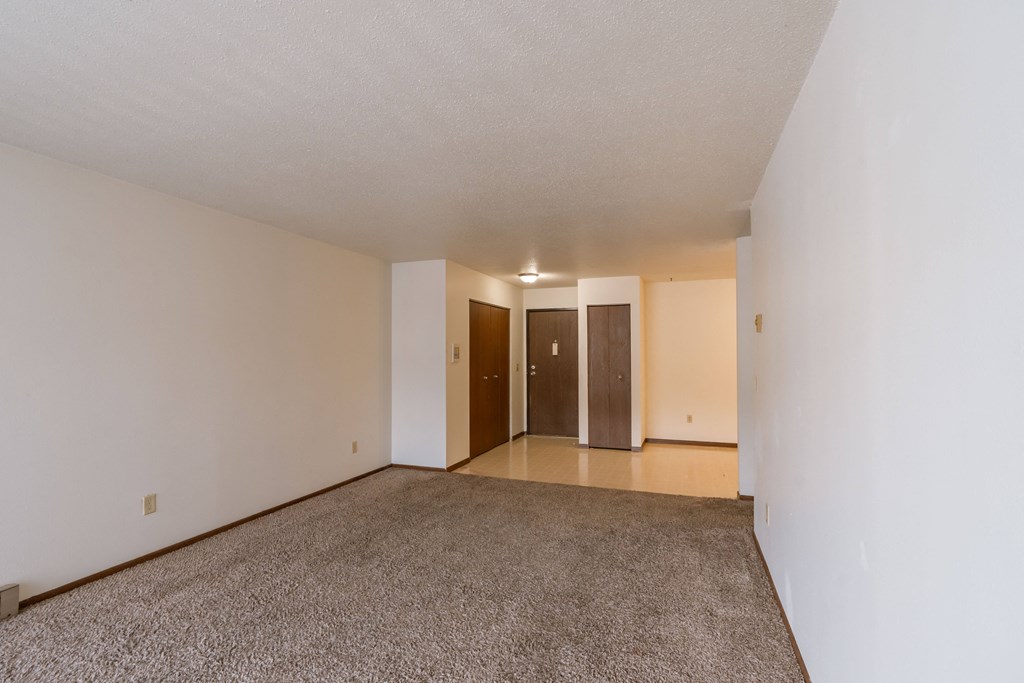 an empty living room with carpet and white walls. Moorhead, MN South Park Apartments