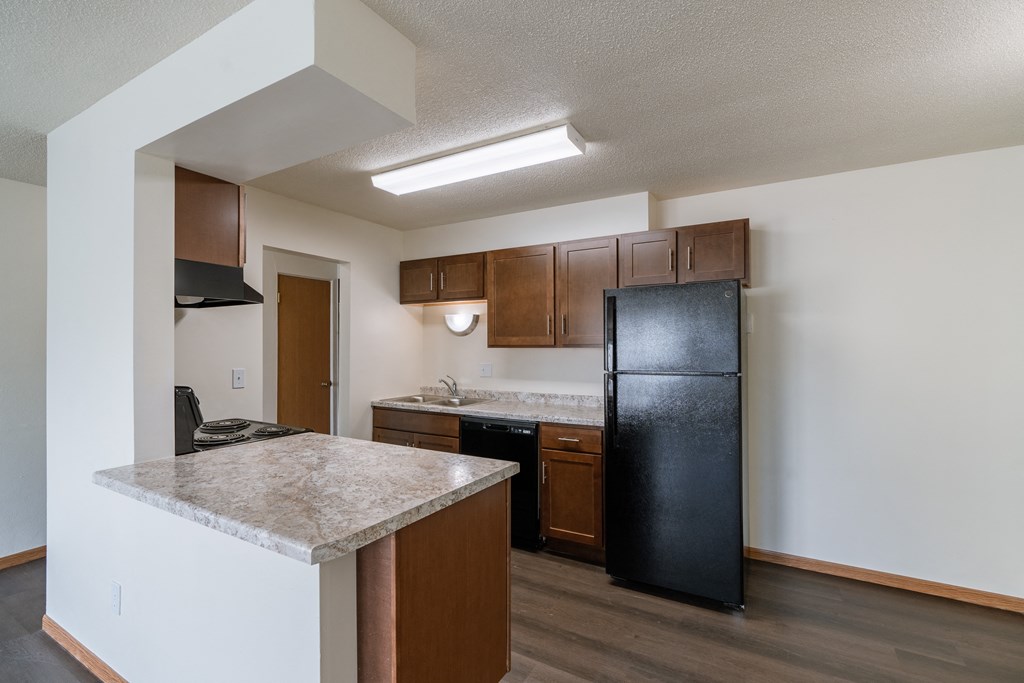 an empty kitchen with a counter top and a black refrigerator. Fargo, ND North Manor Apartments