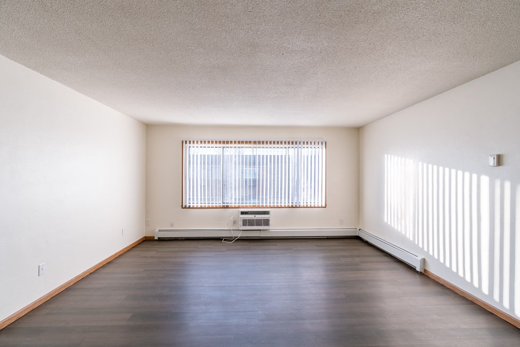 an empty living room with a large window and wood floors. Fargo, ND North Manor Apartments