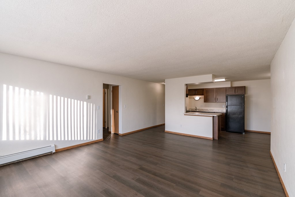 the living room and kitchen of an empty apartment with wood floors and white walls. Fargo, ND North Manor Apartments