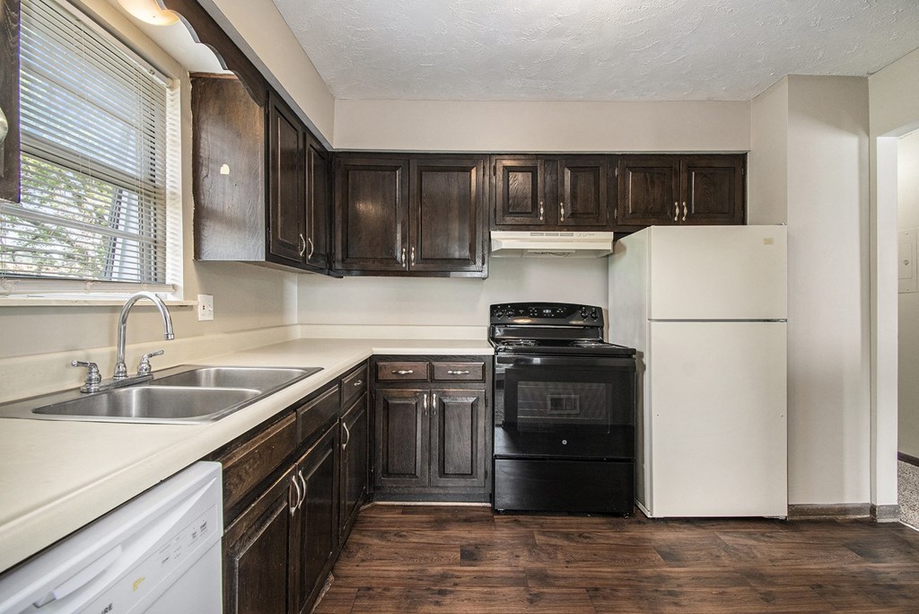 Omaha, NE Beacon Hill Apartments. A kitchen with dark wood cabinets and white appliances