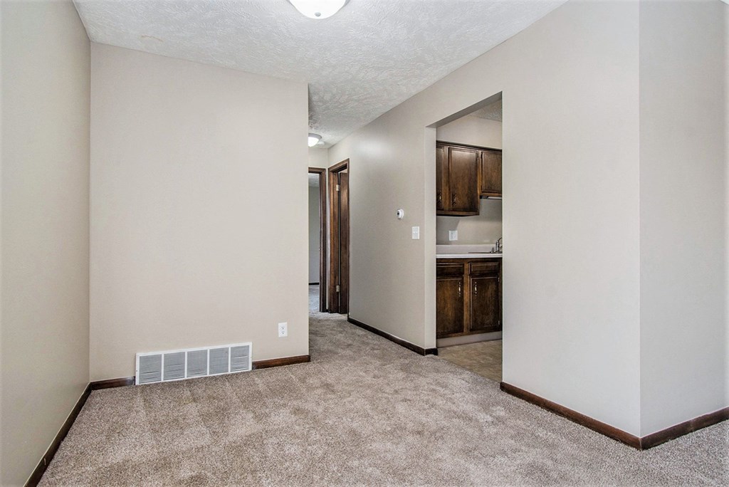 Omaha, NE Maple Ridge Apartments. A living room with a carpeted floor and a kitchen in the background