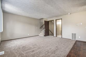 Omaha, NE Stony Brook Townhomes. a living room with a carpeted floor and a staircase in the background - Photo Gallery 3