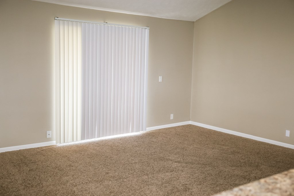 an empty living room with a large window with white blinds. Omaha, NE Evergreen Terrace Apartments