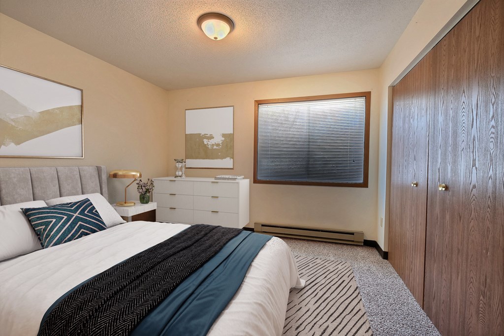 a bedroom with a bed and a dresser and a window. Fargo, ND Prairiewood Meadows Apartments