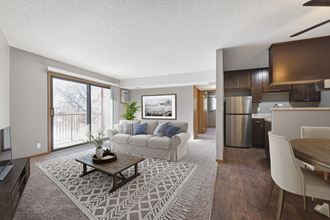 a living room in st louis park at the courtyard apartments with a couch a coffee table and a couch with a kitchen in the background. The large sliding glass door brings bright natural light into the room - Photo Gallery 4