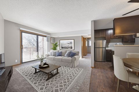 a living room in st louis park at the courtyard apartments with a couch a coffee table and a couch with a kitchen in the background. The large sliding glass door brings bright natural light into the room