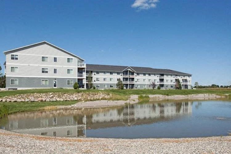 A large building with a pond in front of it. Fargo, ND West Lake Apartments.