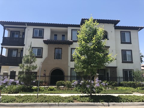 the front of an apartment building with trees and flowers
