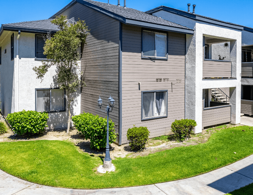 a gray and white building with a lamp post in the middle of a grassy areaat Lincoln Park Apartments, Corona, 92882