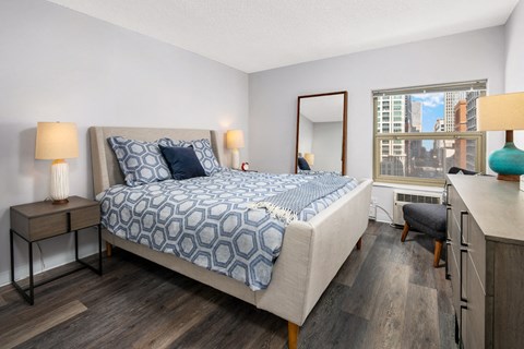 A bedroom with a large bed and a city view through the window.