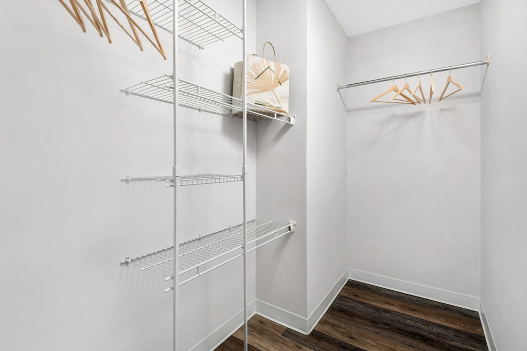 a walk in closet with white walls and shelves and a mirrored closet door