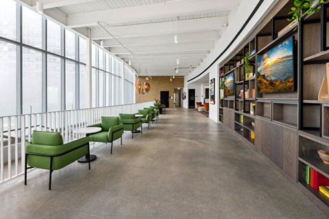 A long hallway with green chairs and a white railing.