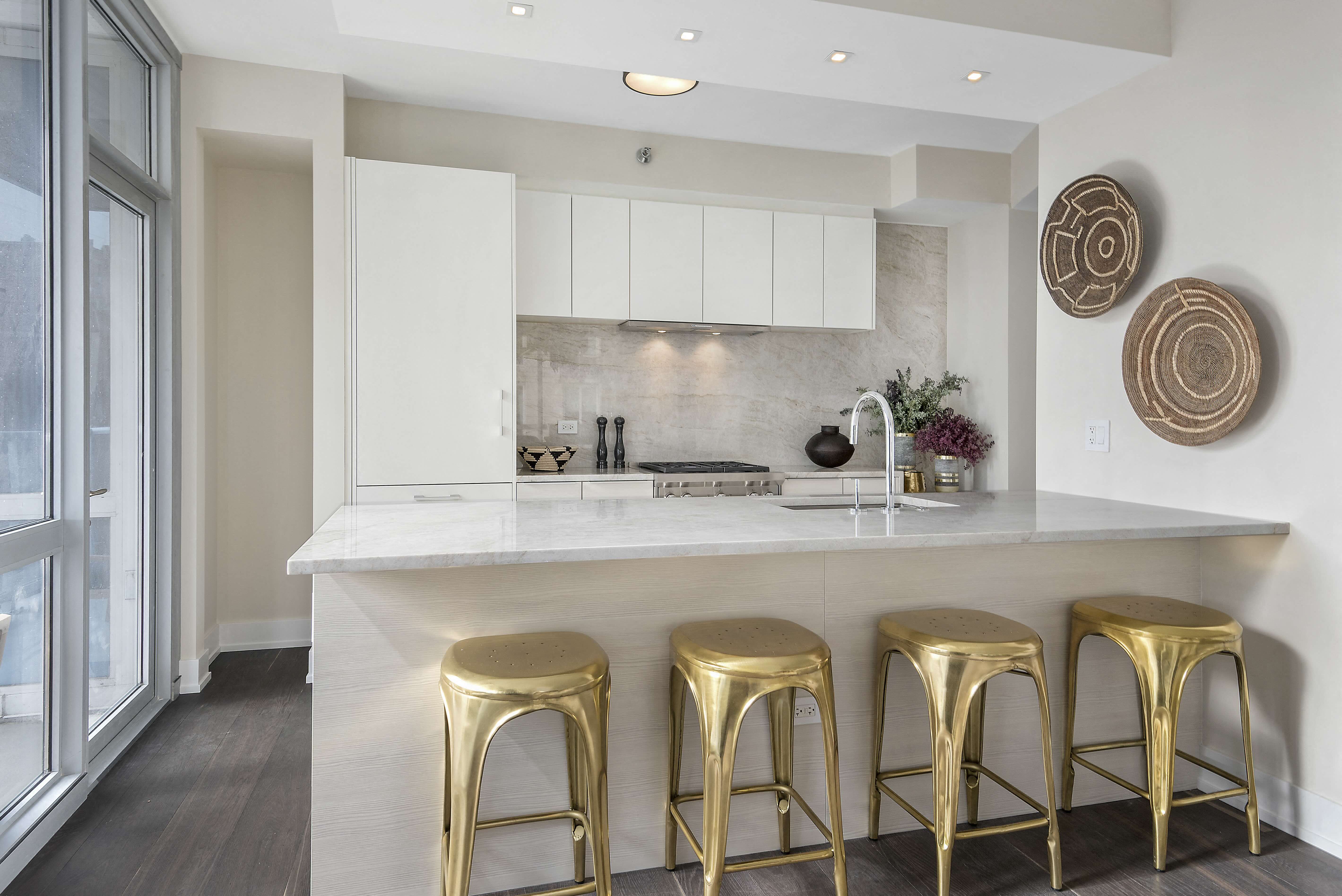 A kitchen with white cabinets and a white countertop with gold stools.