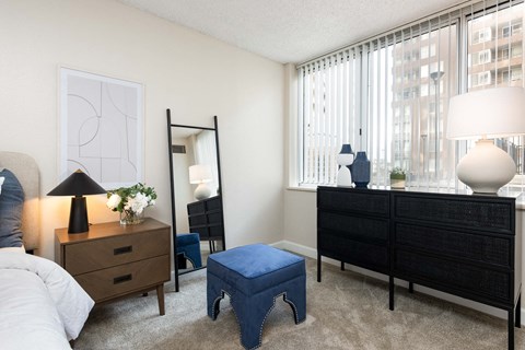 a bedroom with a large window and a bed with a blue ottoman