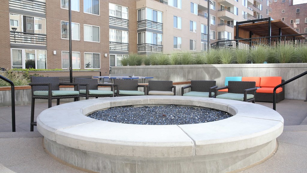 an outdoor seating area with chairs and a fire pit in front of an apartment building