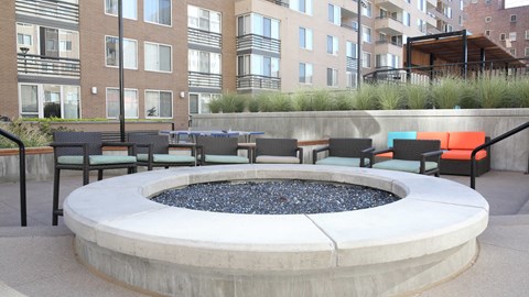 an outdoor seating area with chairs and a fire pit in front of an apartment building