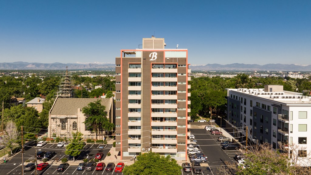 A tall building with the letter B on it is in the middle of a parking lot.