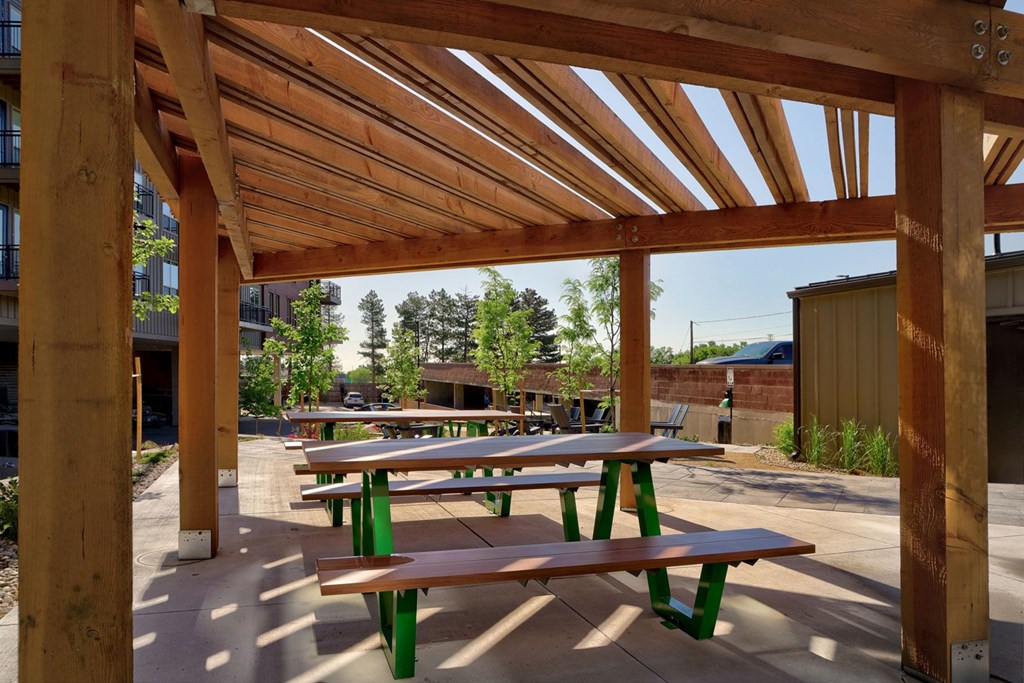 A wooden pergola with green benches is in the foreground.