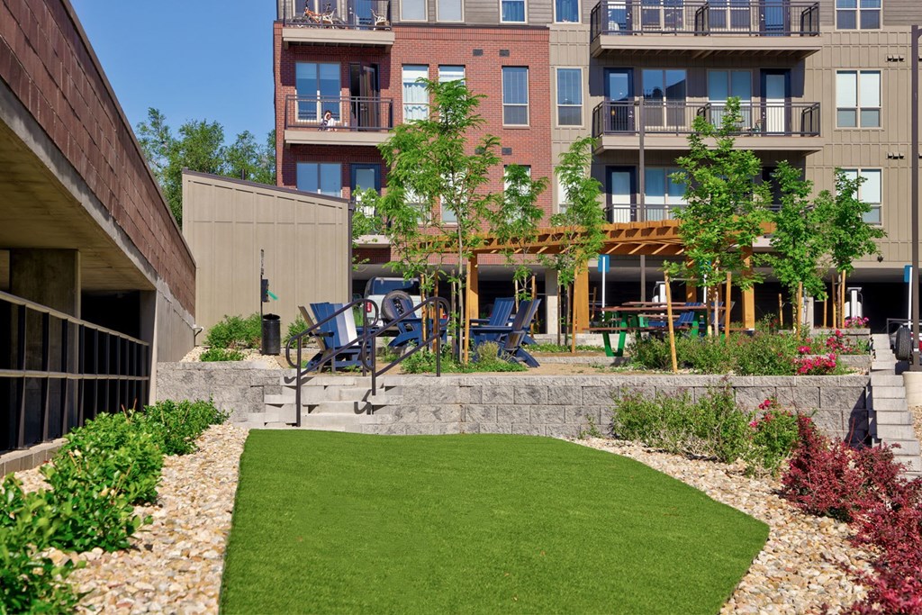 A small grassy area in front of a building with a bench and a tree.