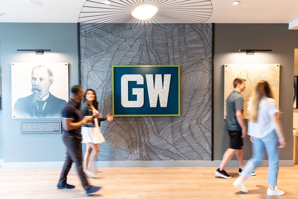 People walking in front of a wall with a GW sign on it.