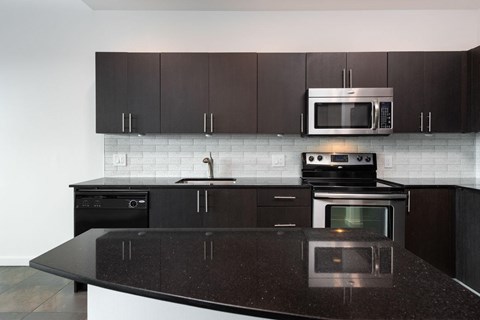A kitchen with a black countertop and a white tile backsplash.