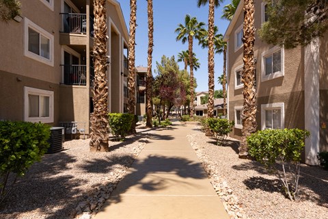 a walkway between two apartment buildings with palm trees
