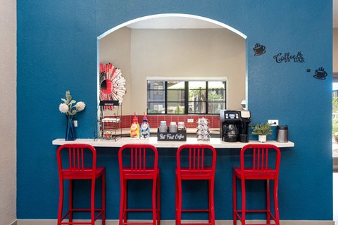 a bar with four red stools in front of a counter with red chairs