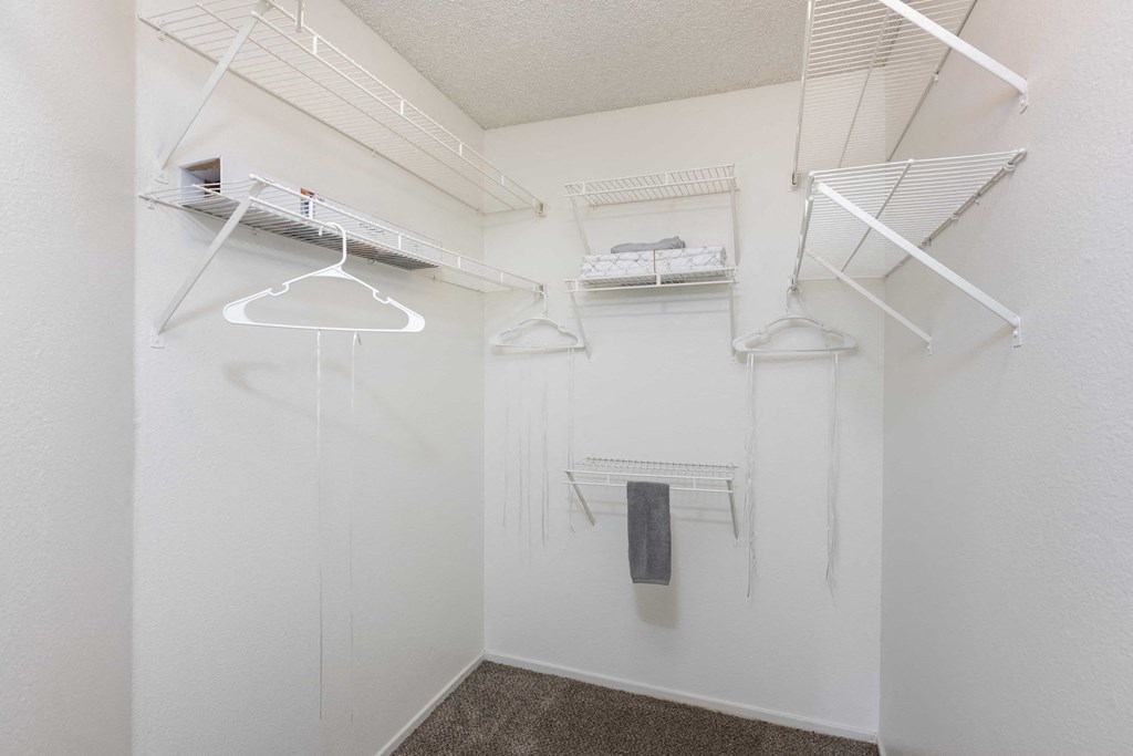a walk in closet with white walls and shelves and hanging racks