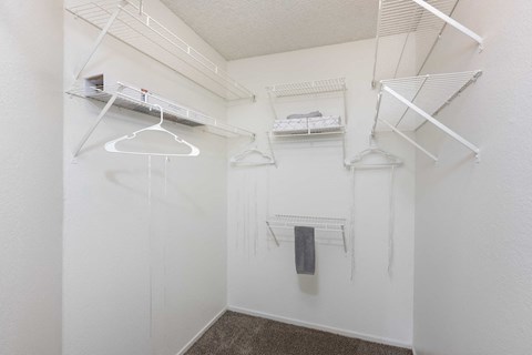 a walk in closet with white walls and shelves and hanging racks