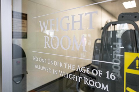 a weight room sign on the door of a gym with escalators