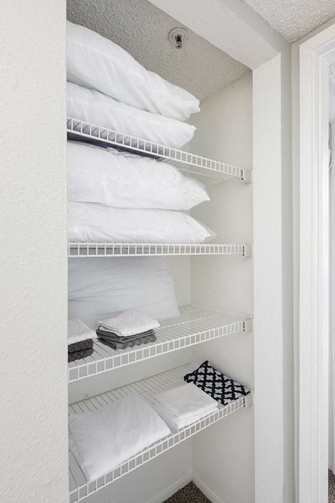 a white closet with shelves filled with folded white towels and pillows