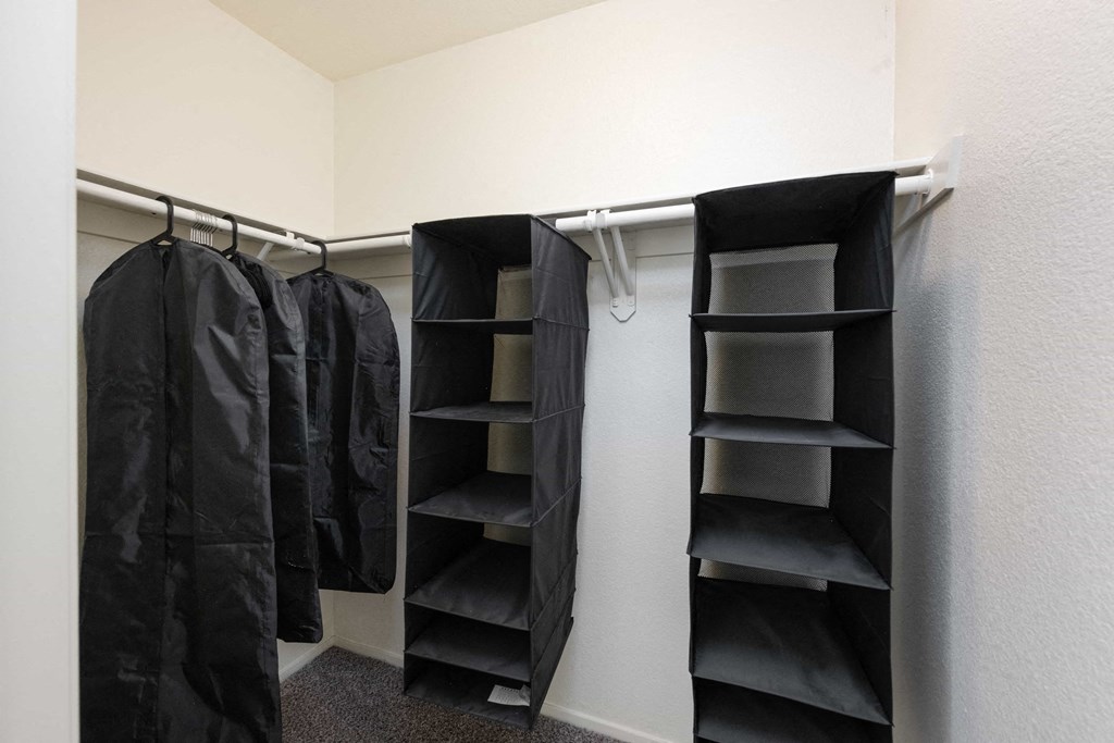 a walk in closet with black jackets and empty shelves