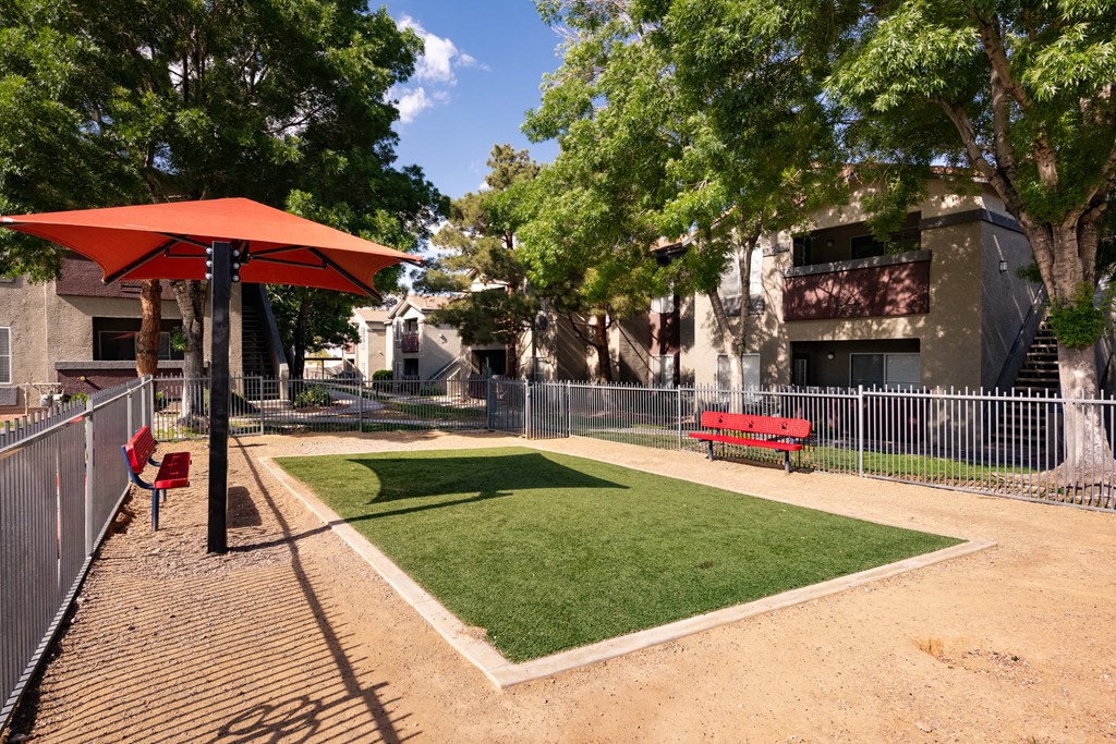 a fenced in dog park with grass and umbrella