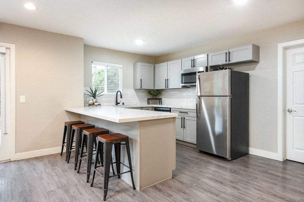 a kitchen with a large island with bar stools and a stainless steel refrigerator