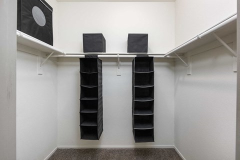 a walk in closet with black shoe racks and a white wall