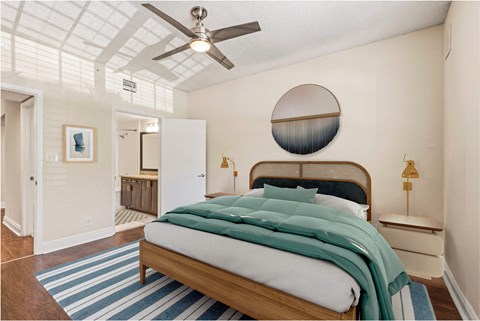 A bedroom with a bed, a ceiling fan, and a round mirror on the wall.