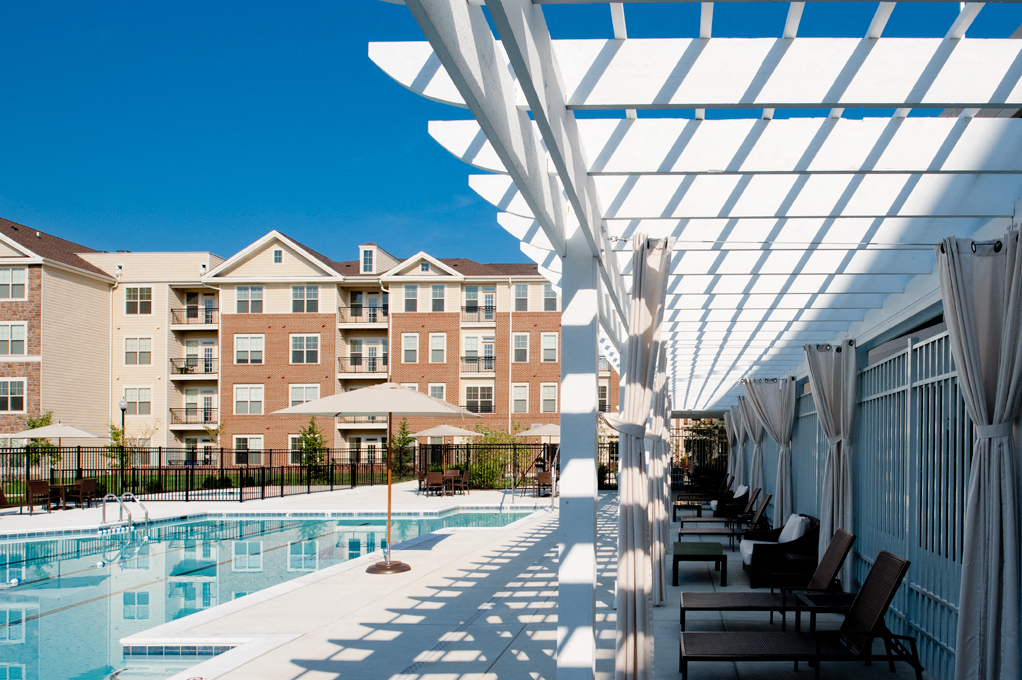 a swimming pool with chairs under a white canopy in front of an apartment building