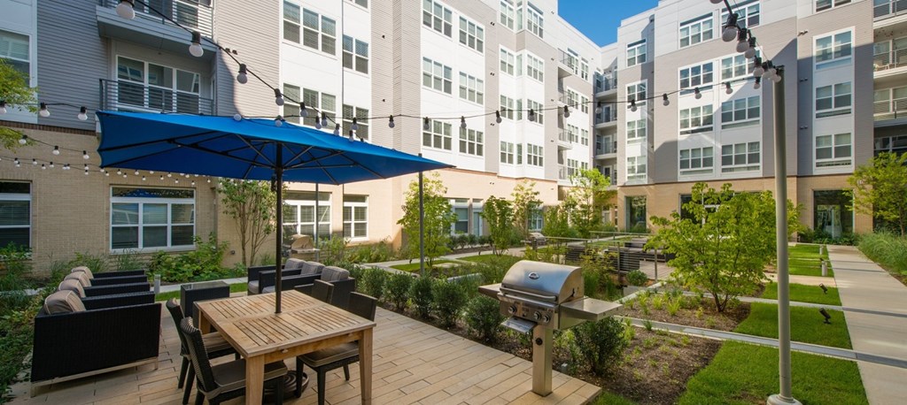 a patio with an umbrella and a table with chairs and a grill at The Metropolitan Downtown Columbia, Columbia, 21044